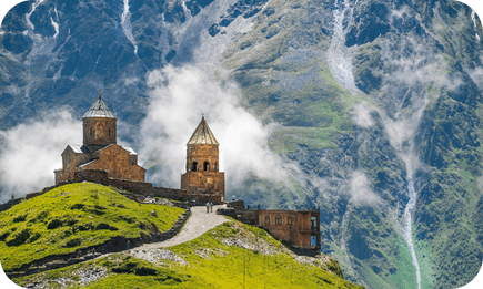 Ancient Georgian church perched atop green mountains shrouded in mist.